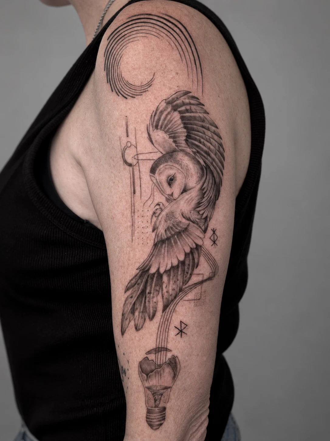 Barn owl in flight with geometric linework and a light bulb, tattooed on the upper arm