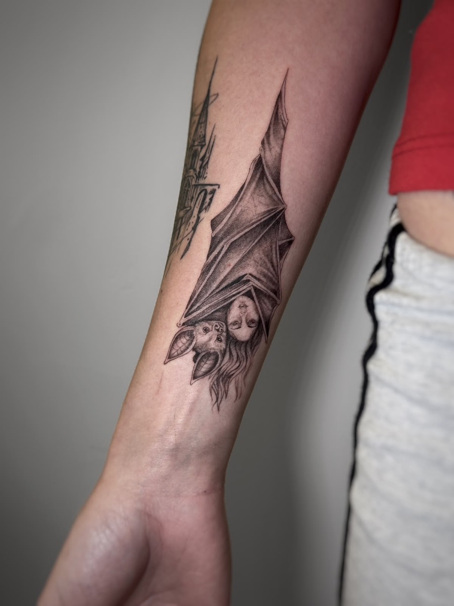 Realistic bat hanging with open wings, tattooed on the forearm
