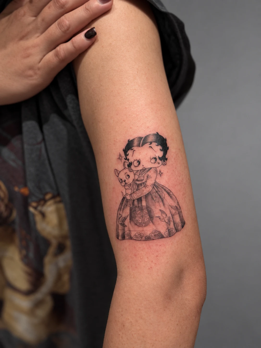 Betty Boop in a Korean hanbok holding a small dog, tattooed on the back of the arm
