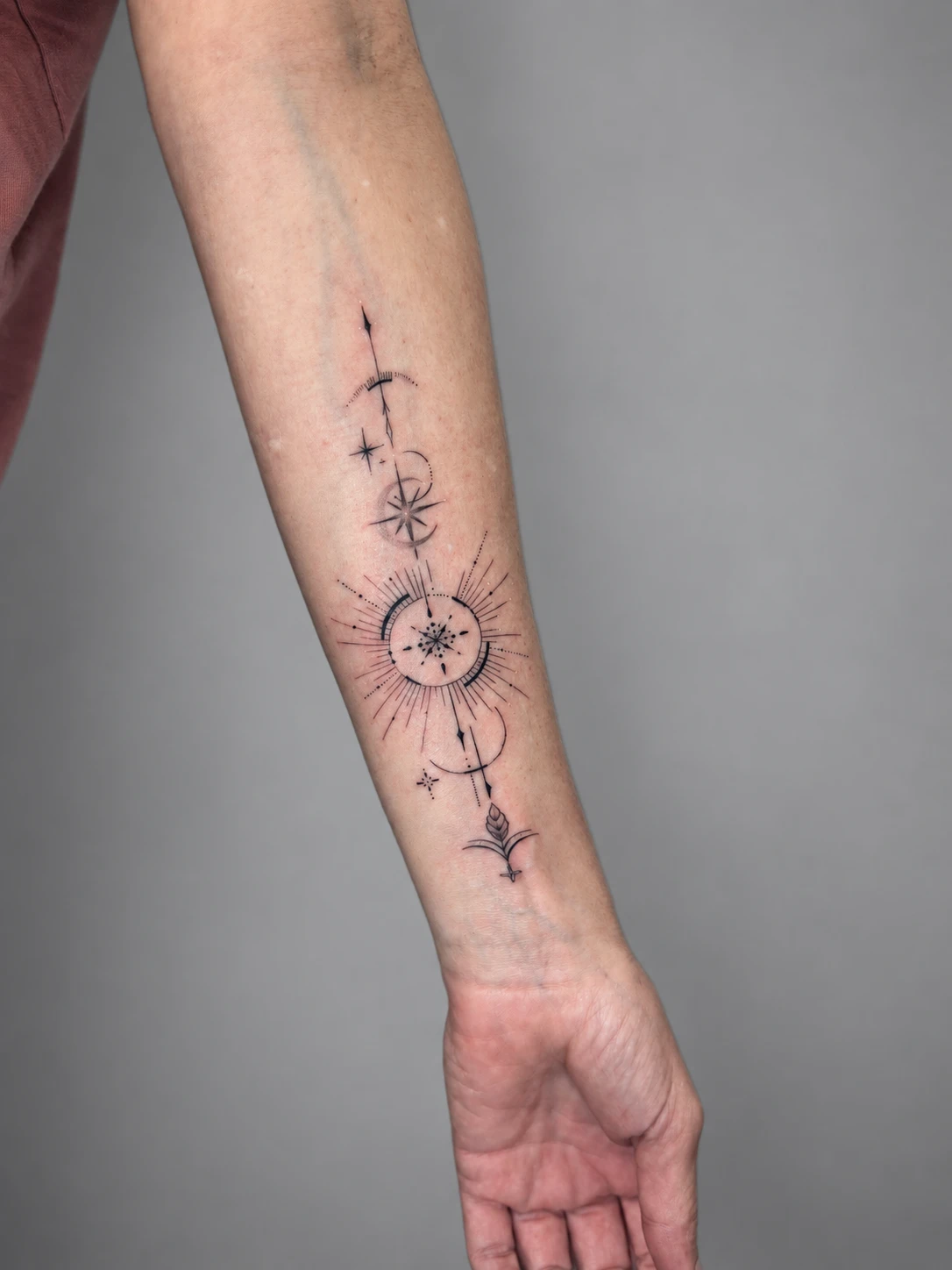 Fine-line celestial arrow with a sun, moons and stars on the inner forearm