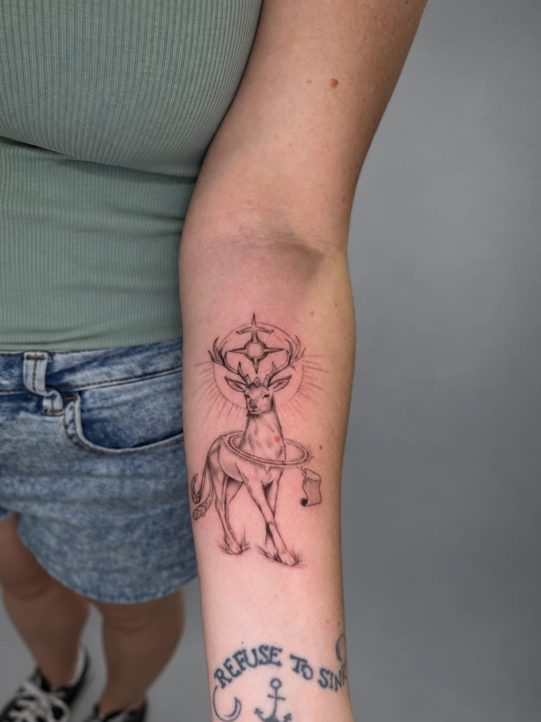 Fine-line stag crowned with a compass star and halo on the inner forearm