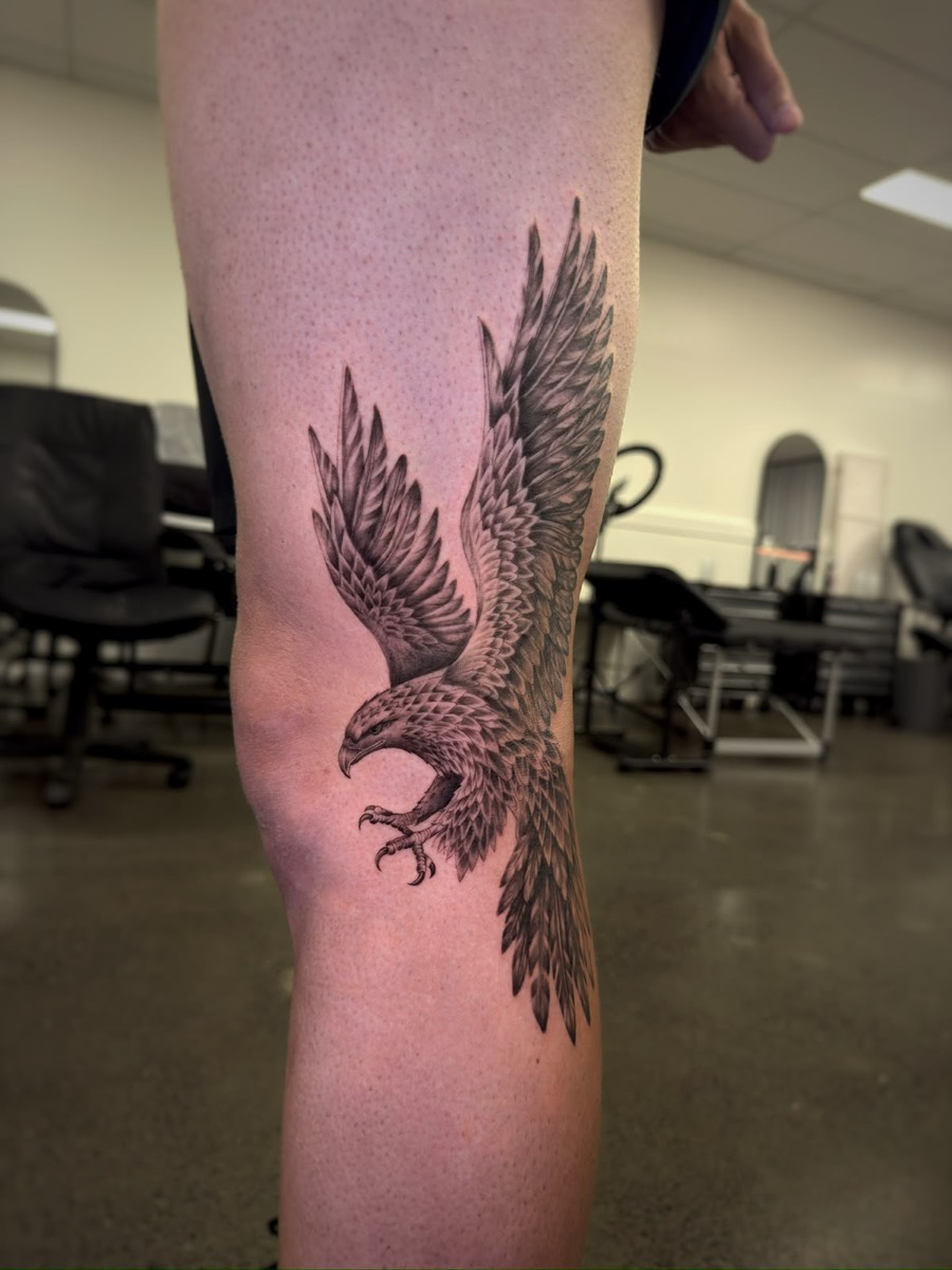 Realistic eagle landing with open talons, tattooed above the knee