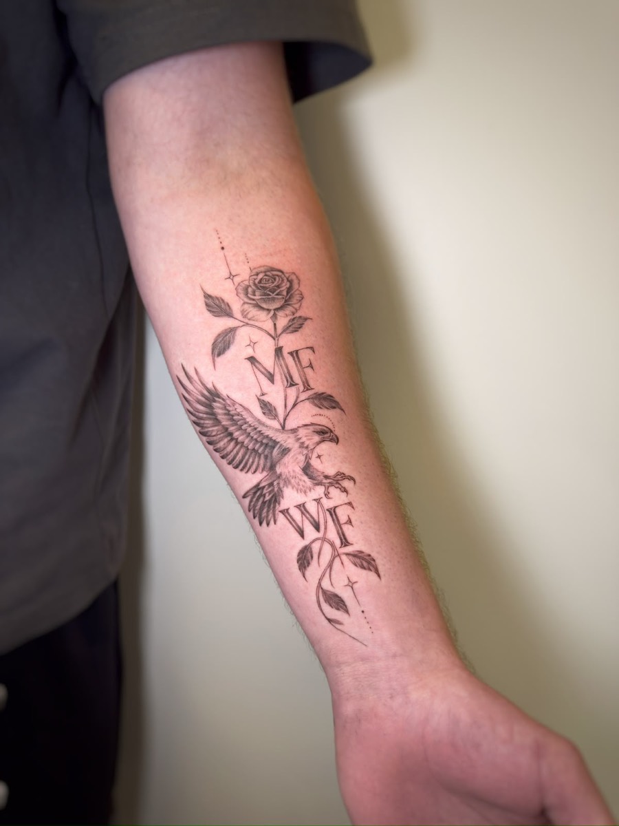 Fine-line forearm tattoo with a rose, an eagle in flight and the initials MF and WF